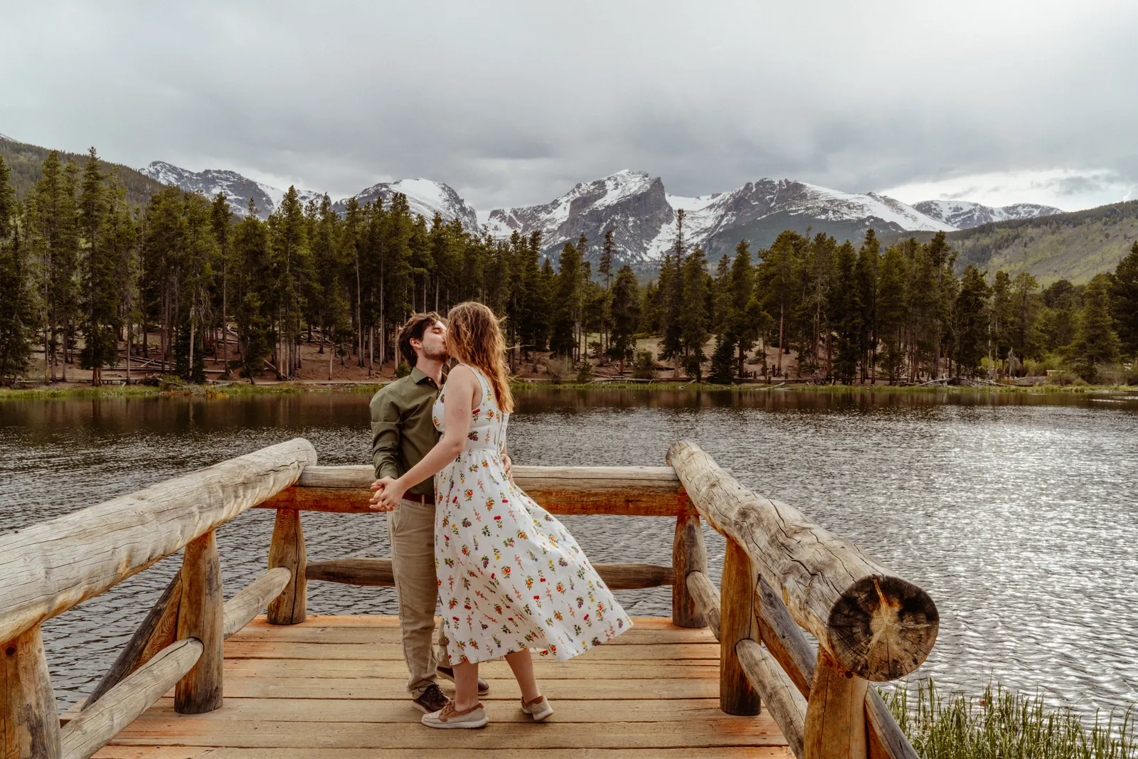 Couple on a lakeside bench beneath snow-capped peaks, engagement session in Rocky Mountain National Park