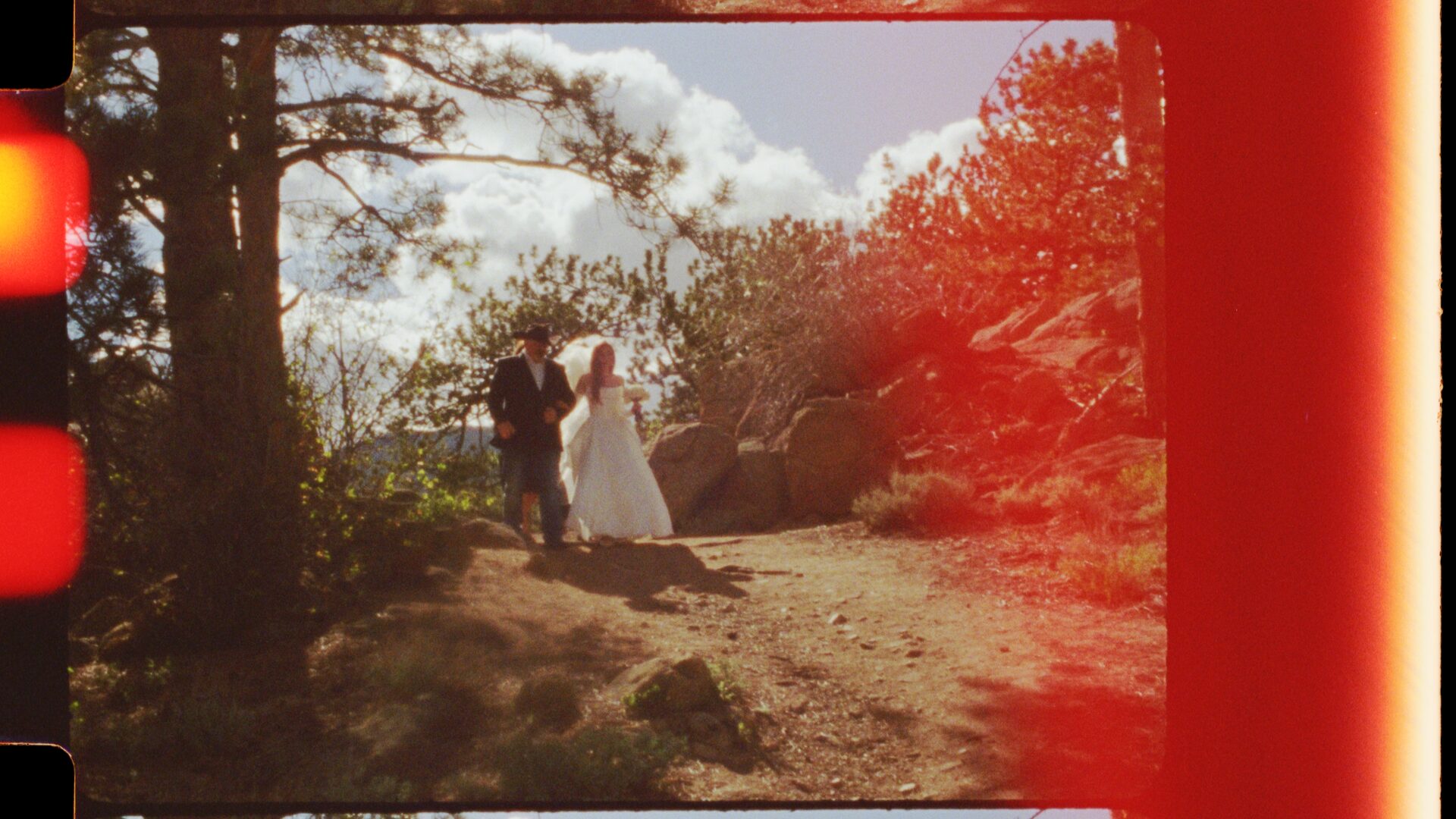 Wide trail shot of a couple at Rocky Mountain National Park with a warm 16mm film light leak across the frame