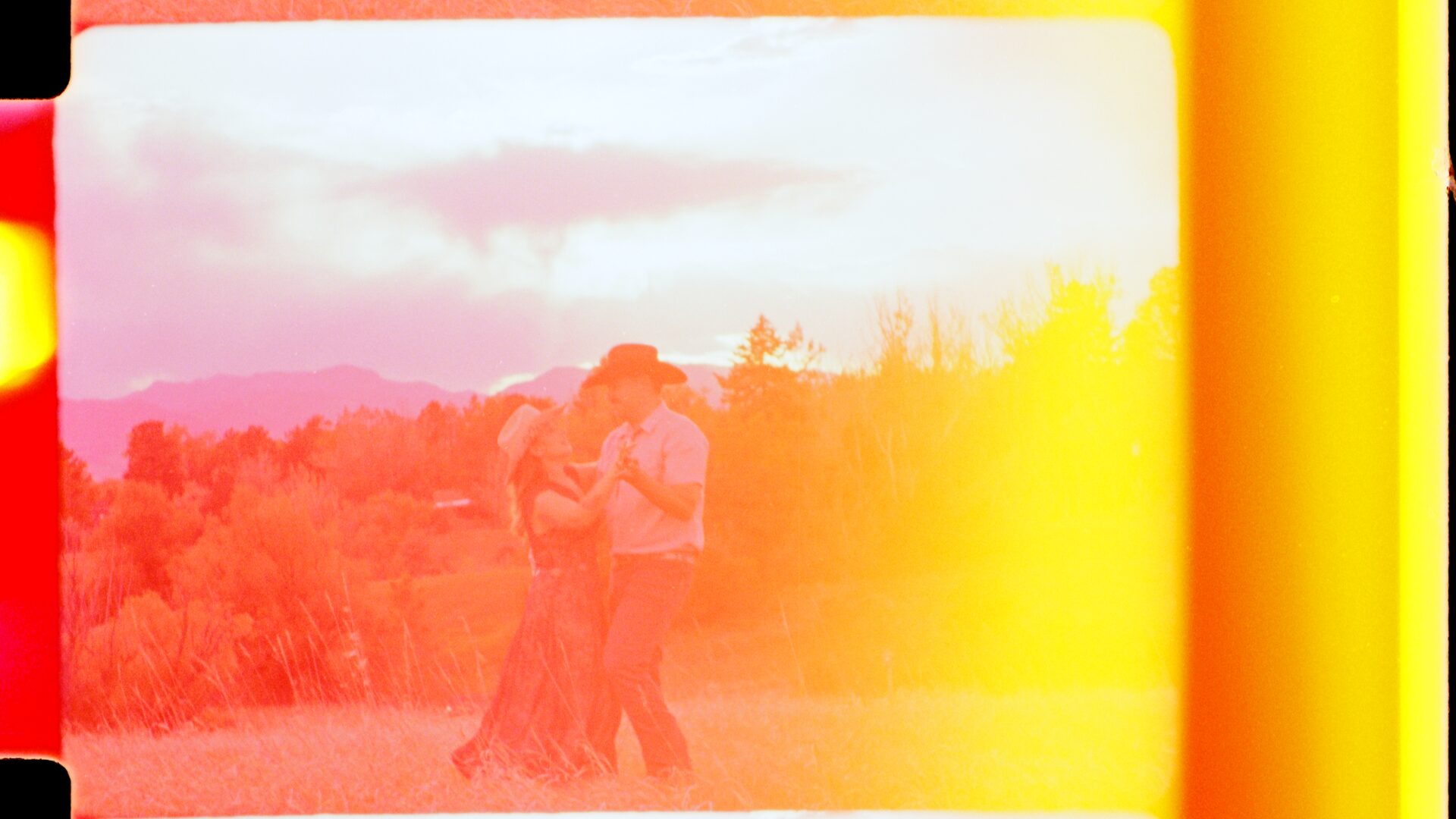 16mm film still — Kesia and Brian during their Colorado engagement session, a warm orange light leak washing across the frame. This is real film reacting to light — not a filter applied in post.