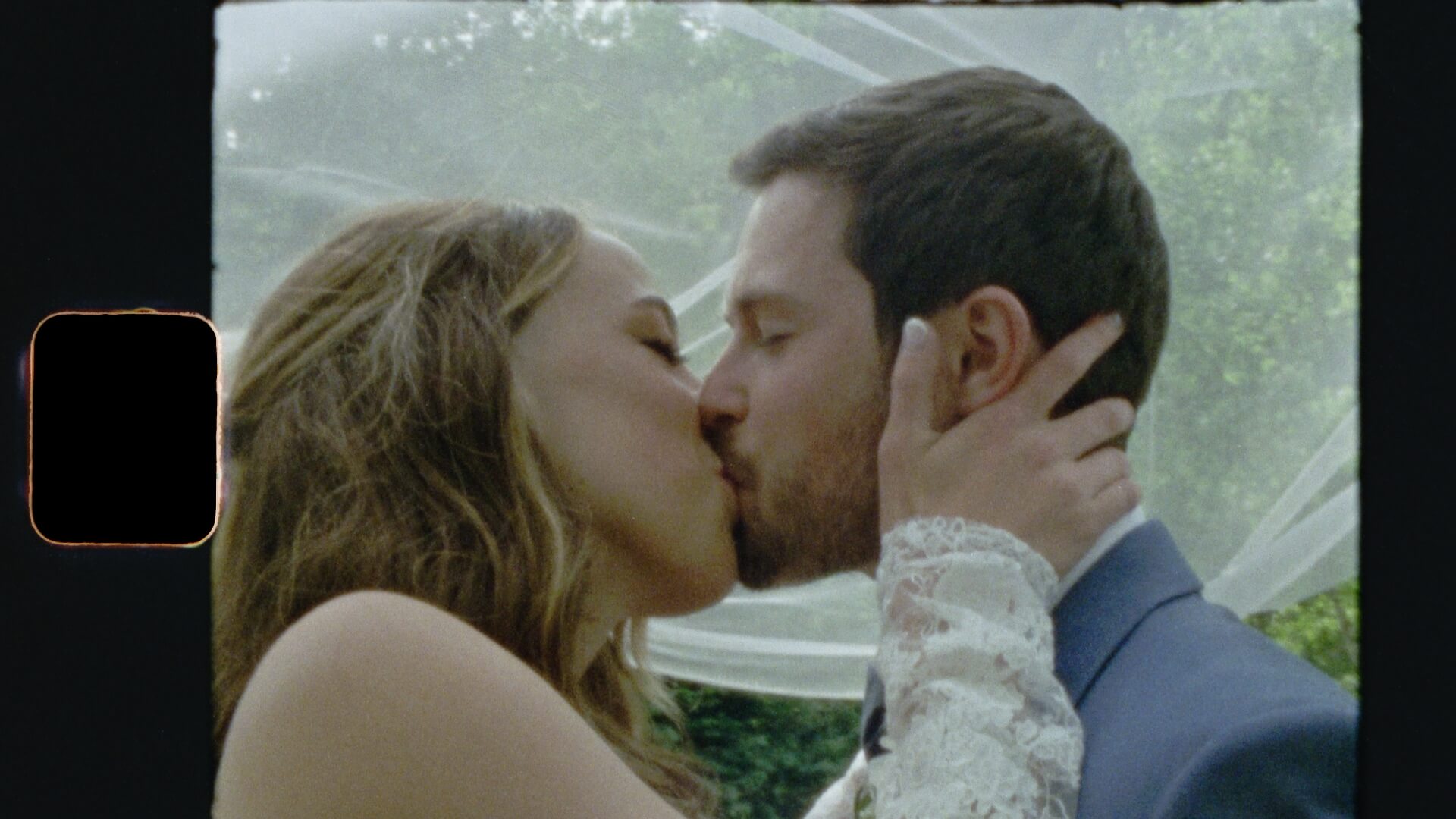 Super 8mm wedding film frame — couple sharing a first kiss under the wedding veil, lush green garden behind them. Film grain, Kodak color rendering, and the soft motion blur of 18fps — the look that defines the Super 8mm aesthetic.